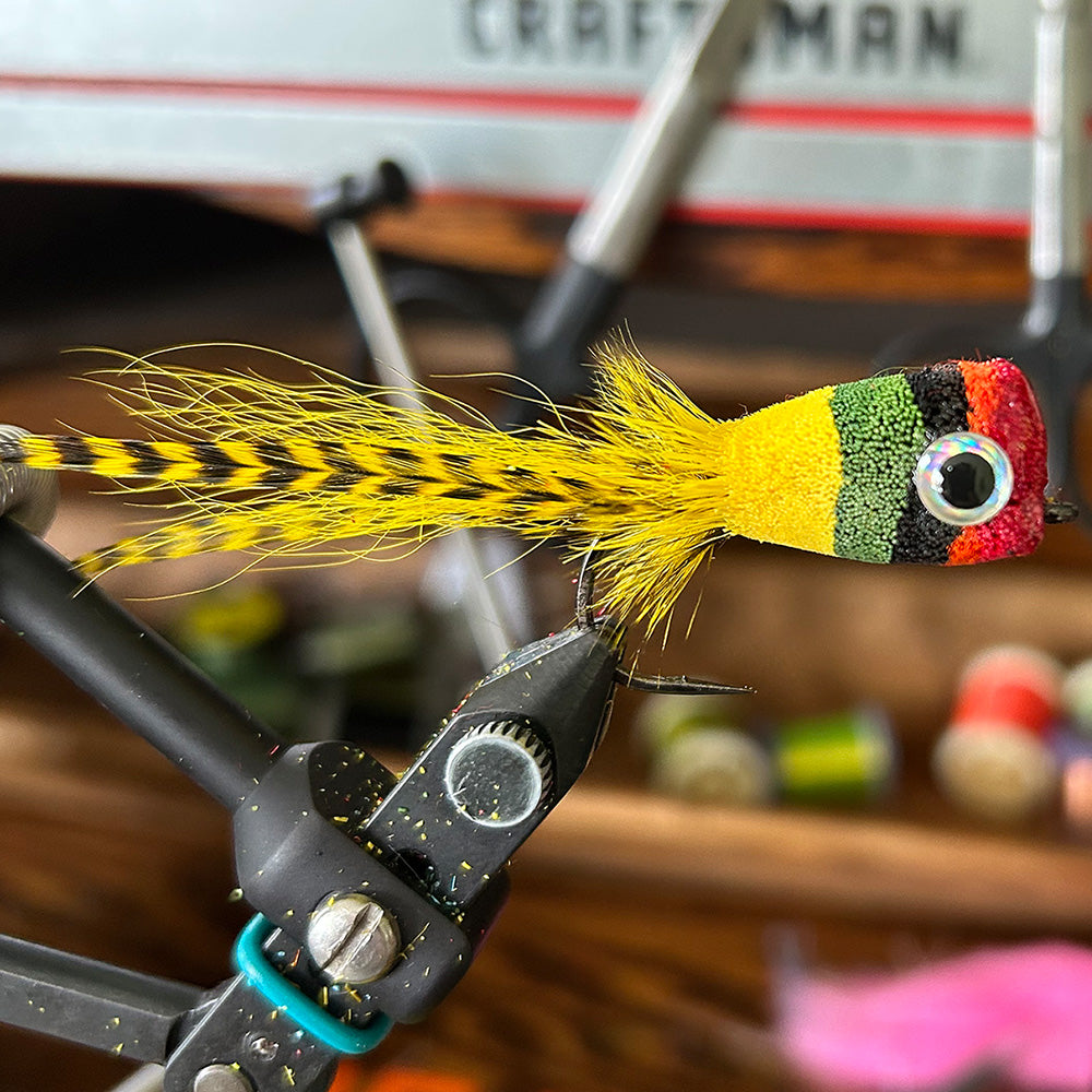 pictured is a well tied deer hair bass bug in green, red, black and yellow with eyes