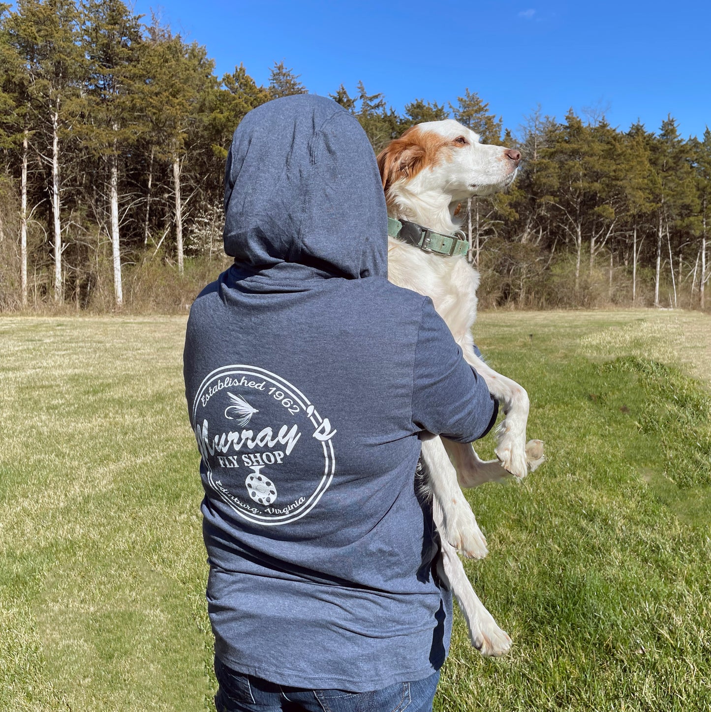 Hooded sun shirt with a Murray's Fly Shop logo on the back. Girl has the hood up and is holding a Brittany spaniel dog