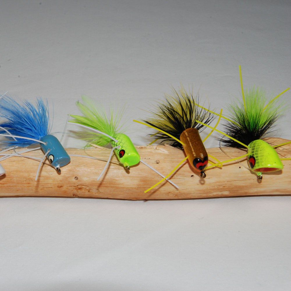 hand-tied bass popper for fishing sitting on a piece of driftwood on a grey background