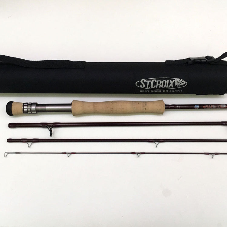 Shown is a used St. Croix fly rod lying on a white background with the handle, reel seat, and four pieces of the graphite fly rod showing along with the fly rod case