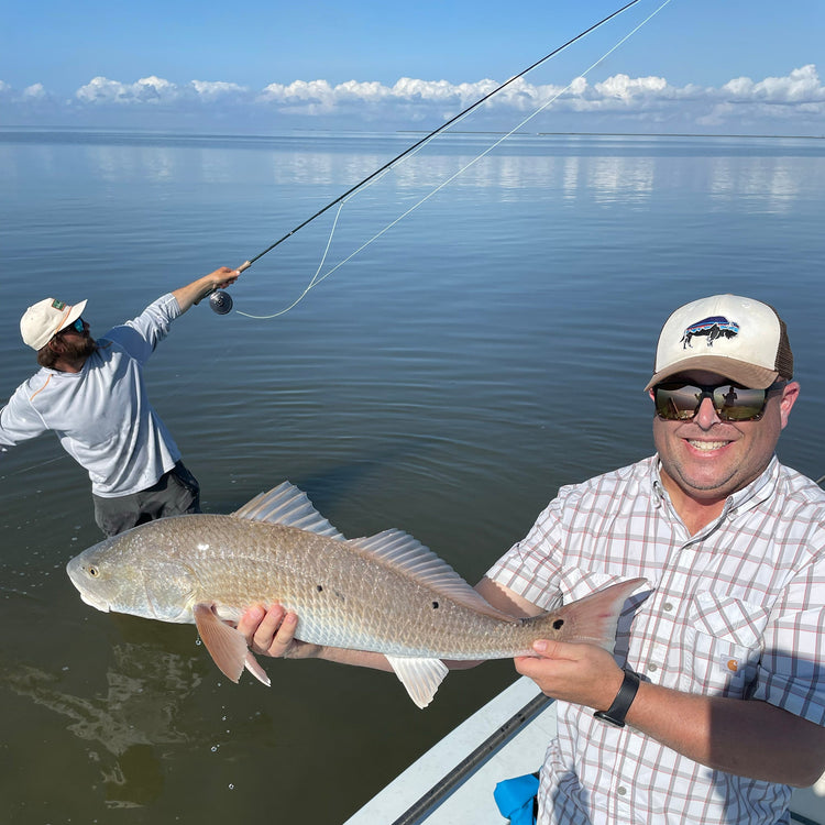 An enthusiastic fly fishing guide standing in the water with a fly rod in his hand and a happy angler holding a redfish - Saltwater fly rod and reel outfits 