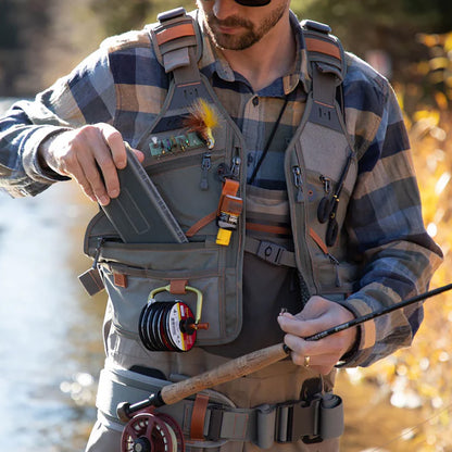Fishpond Flint Hills fly fishing vest shown with accessories on an angler who is putting a fly box in his vest pocket