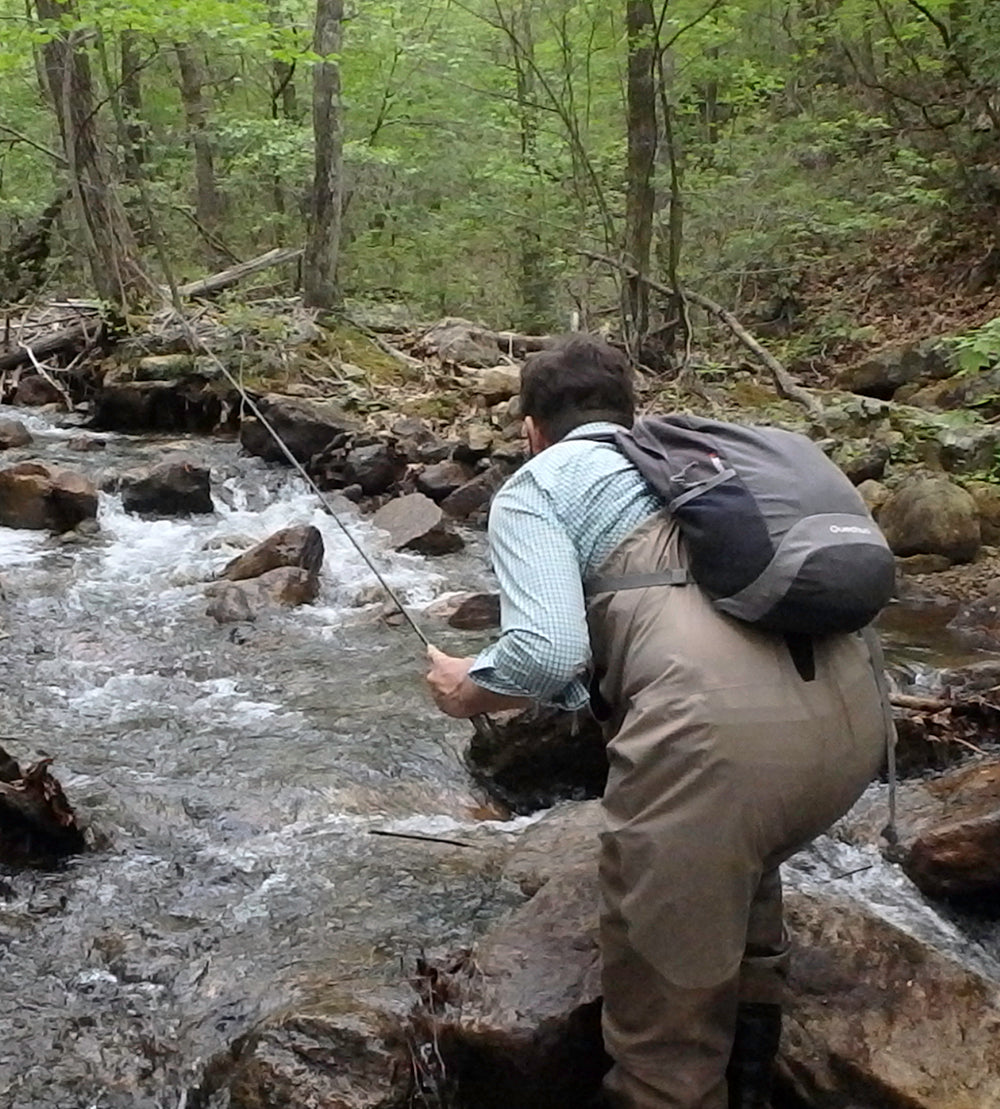 A fly fishing angler stands in a rock filled stream holding a fly rod fishing for native Virginia brook trout in the George Washington National Forest near Edinburg, VA