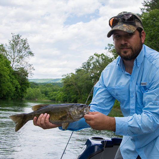 Angler holding a smallmouth bass on the Shenandoah river with the Massanutten Mountains in the background
